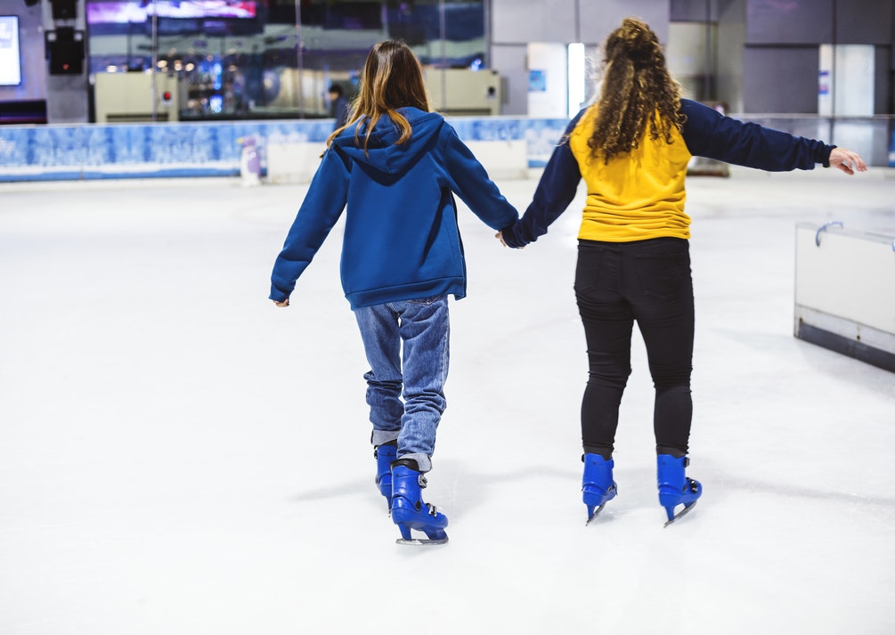 Two girls ice skating at an indoor ink. 