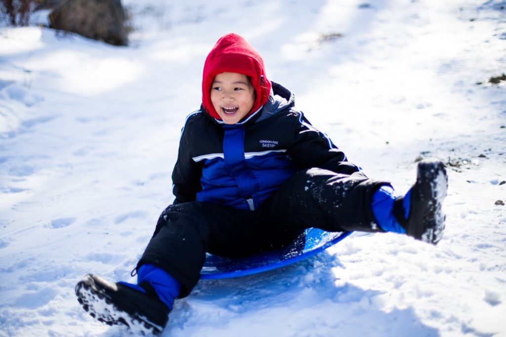 A little kid sledding down a snow hill.